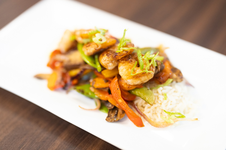 A delicious stir-fry dish featuring perfectly cooked shrimp, vibrant bell peppers, snap peas, and mushrooms, all served over a bed of fluffy white rice. This savory meal highlights the gourmet dining options available at the senior living community restaurant.