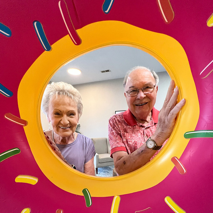 Residents at the senior living community enjoying a playful moment, captured through the hole of a colorful inflatable donut, bringing joy and smiles to their faces.