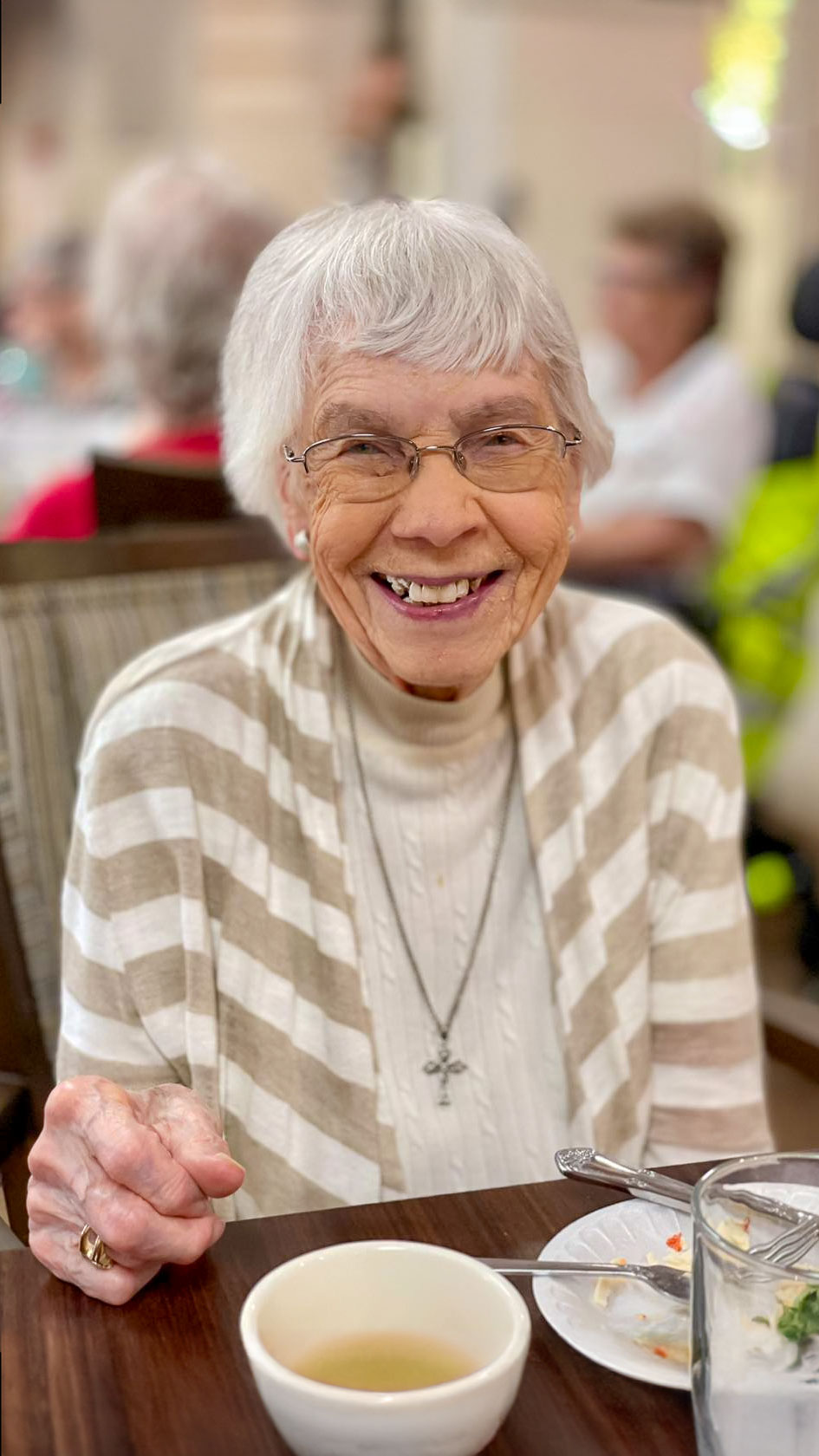 A senior living resident enjoys a meal, smiling warmly at the camera, embodying the welcoming and joyful atmosphere of the community.