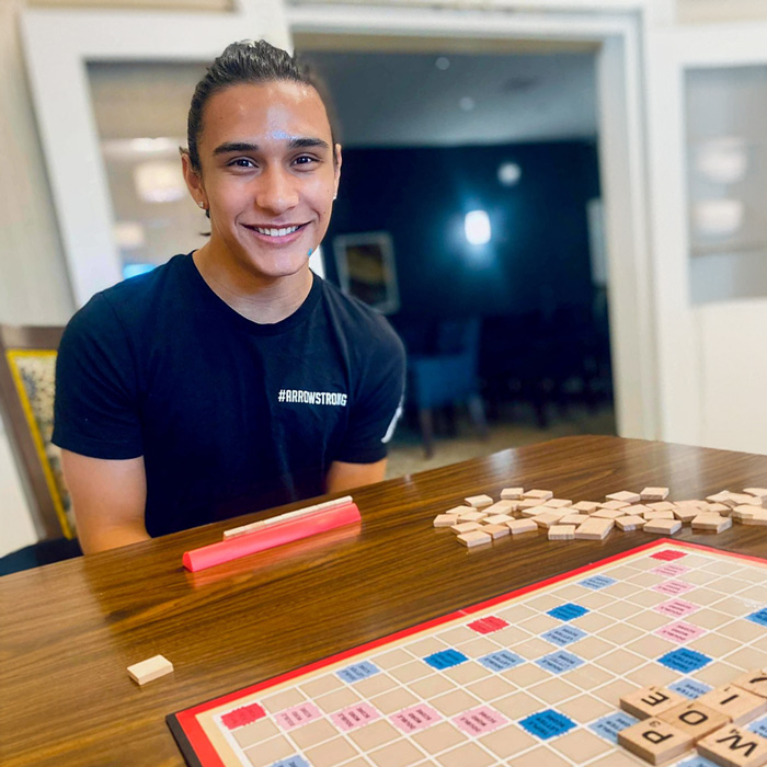 Young man, an employee team member with a black shirt that says '#ArrowStrong,' playing a fun game of Scrabble with senior residents.