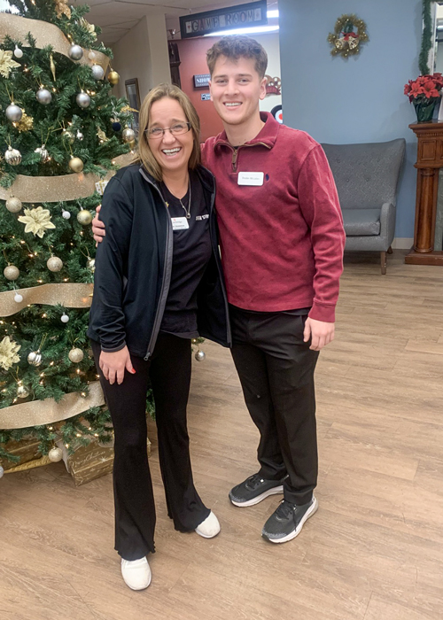 Two team members at a senior living community standing near a decorated Christmas tree, smiling warmly, and wearing professional name tags.