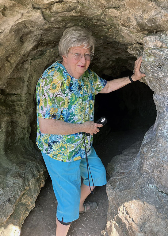Senior woman poses for a photo opportunity at the opening of a cave during an outing.