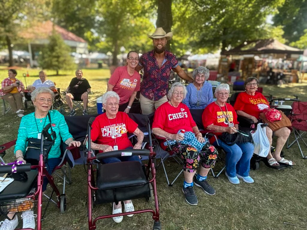 A group of residents from The Cambridge Senior Living, seated outdoors with big smiles at a local celebration.