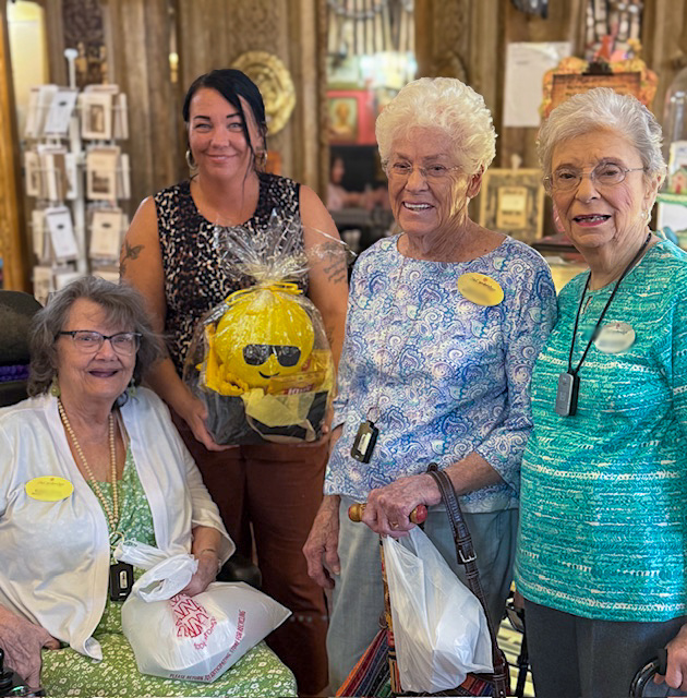 Three senior women from The Cambridge Senior Living present a gift basket to a local business owner.