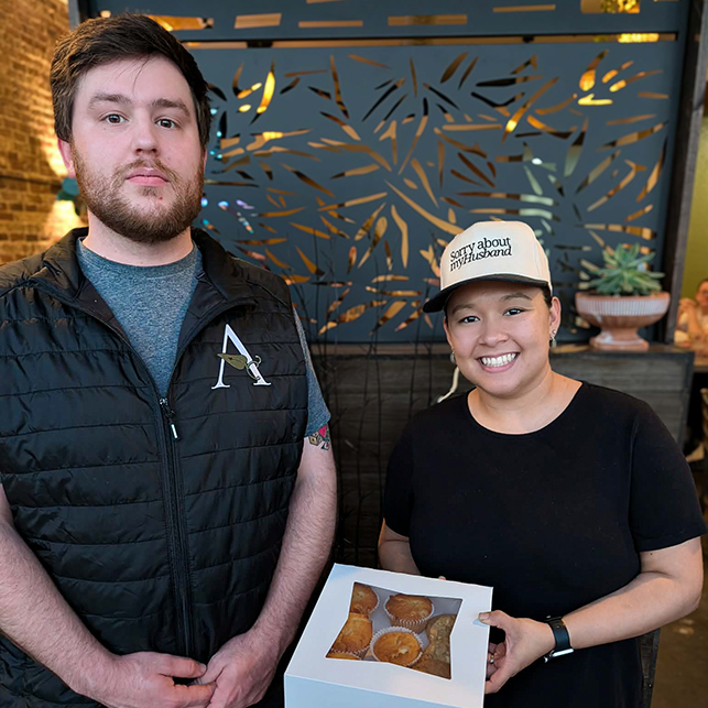 A Cambridge Senior Living team member presents a box of desserts to a smiling local business owner of a fusion restaurant.